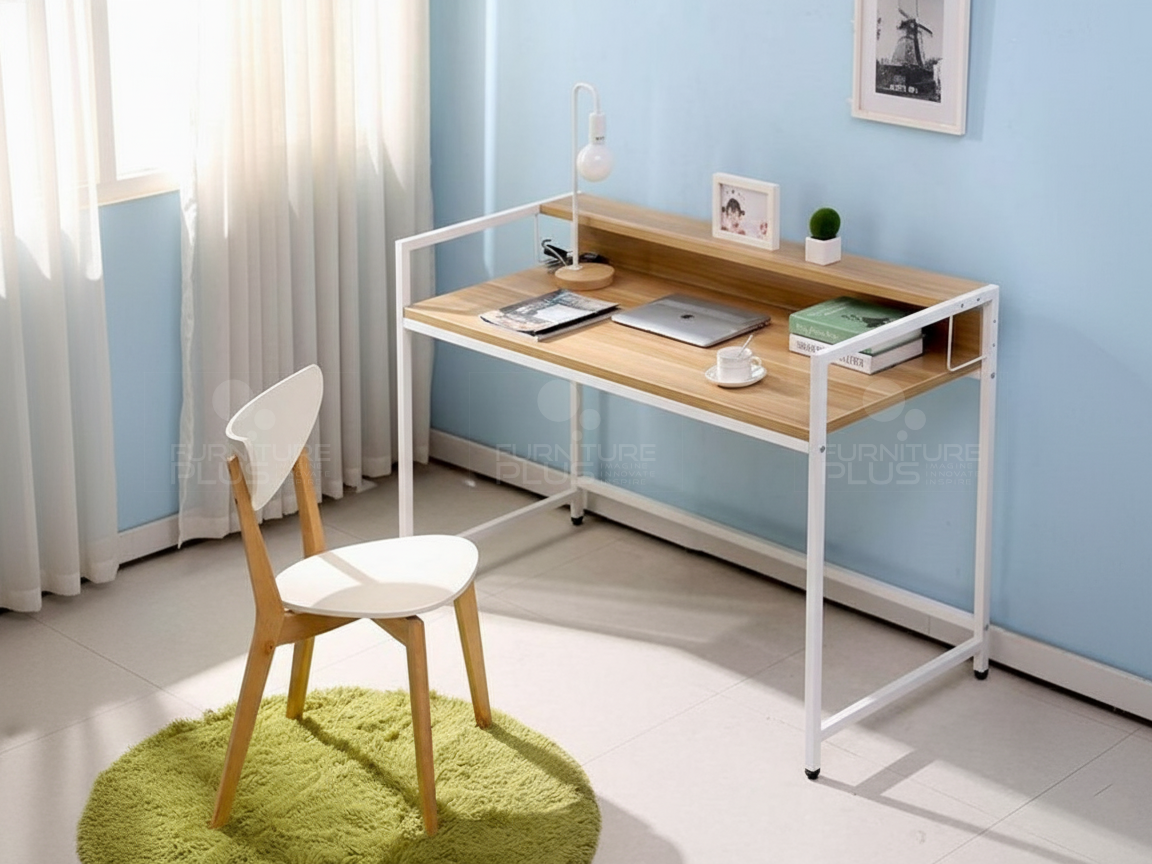 A modern Apollonius writing desk with a light Mahogany wood top and white metal frame, featuring a built-in riser shelf. The desk is staged with a laptop, books, and a lamp against a light blue wall, next to a window with sheer curtains. A white chair with wooden legs sits on a green, circular shag rug in front of the desk
