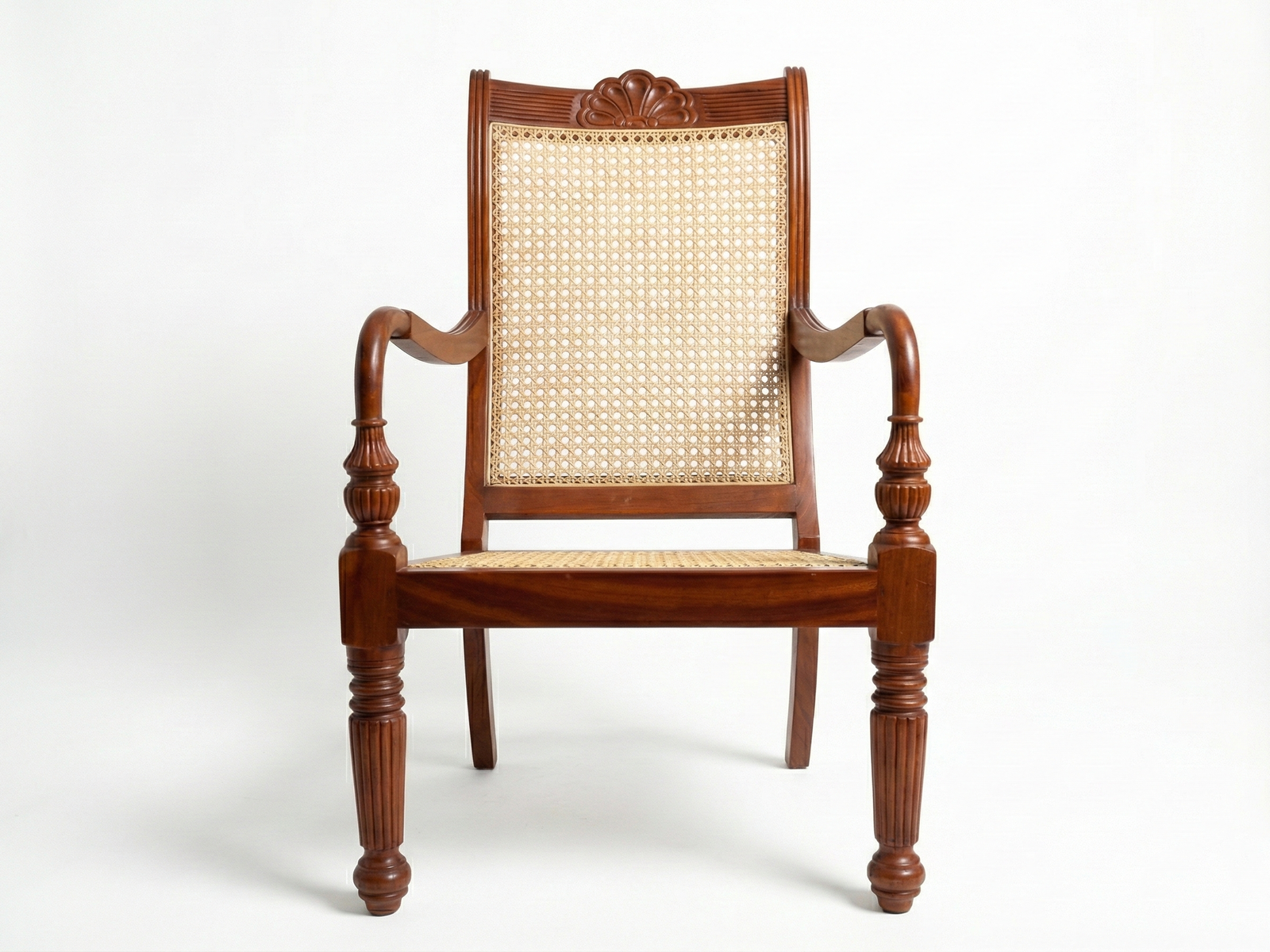Front view of the Caroline Easy Chair, a traditional colonial or plantation-style chair made of polished dark brown Mahogany wood. The chair features an intricately carved wooden crest rail at the top, a caned (woven rattan) back panel, and a matching caned seat. It has decorative turned front legs and scrolled wooden armrests, giving it an elegant, historic appearance. The chair is placed against a plain white background
