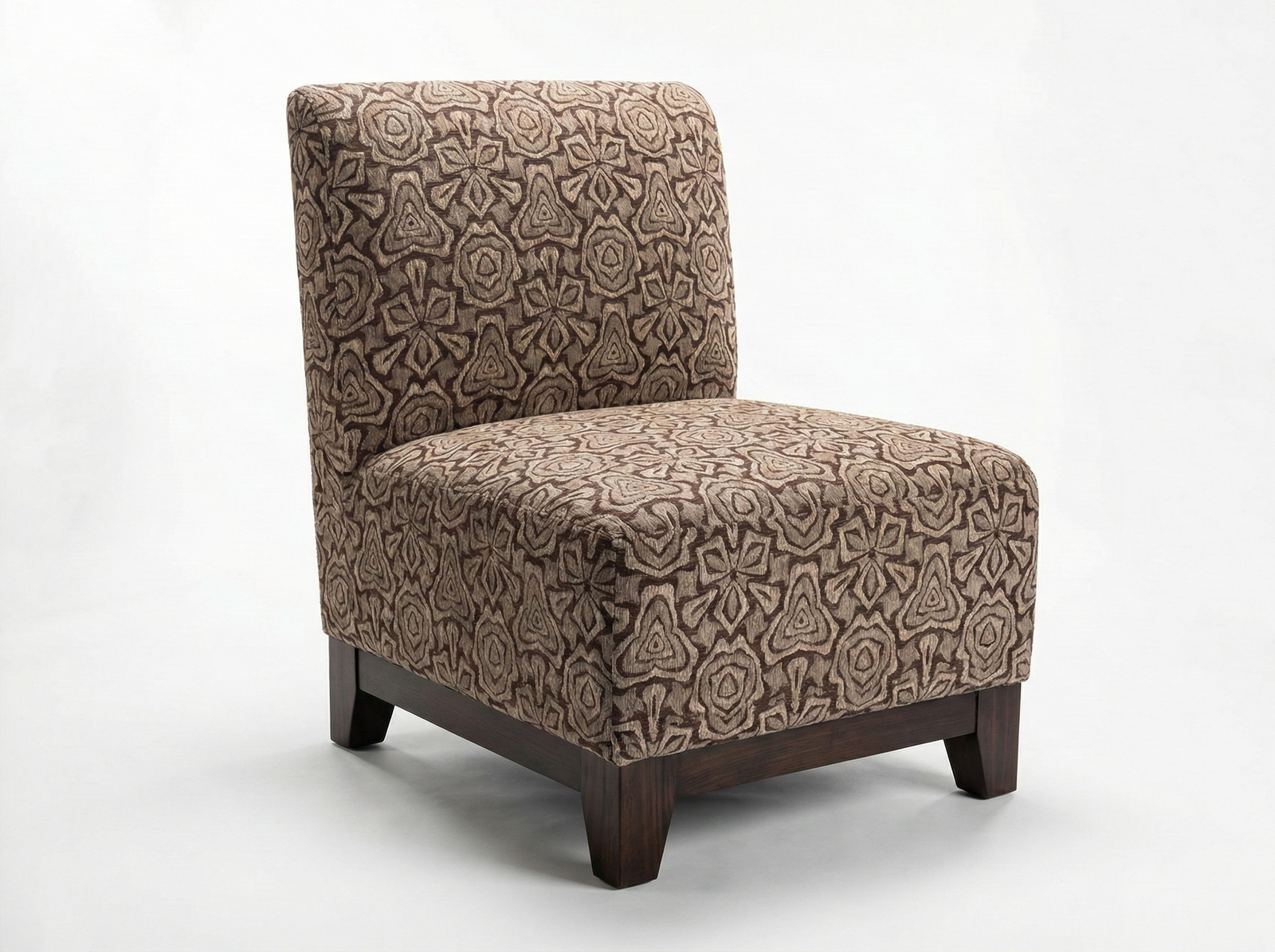 Side view of the Molly Easy Chair, a contemporary, armless slipper chair with a high, squared back. It is fully upholstered in a textured fabric featuring a bold, geometric or kaleidoscope-like pattern in shades of brown and tan. The chair has a low profile and sits on a dark wooden block base with short, sturdy feet, against a plain white background