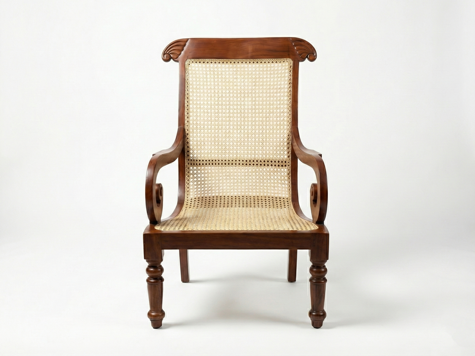 Front view of the Toyo Easy Chair, a traditional colonial or plantation-style chair made of polished dark Mahogany wood. The chair features a high back with a decorative, carved crest rail and has scrolled, turned front legs. The back and seat are both panelled with tightly woven cane (rattan). The arms sweep down and scroll outward at the front. The chair is positioned against a plain white background