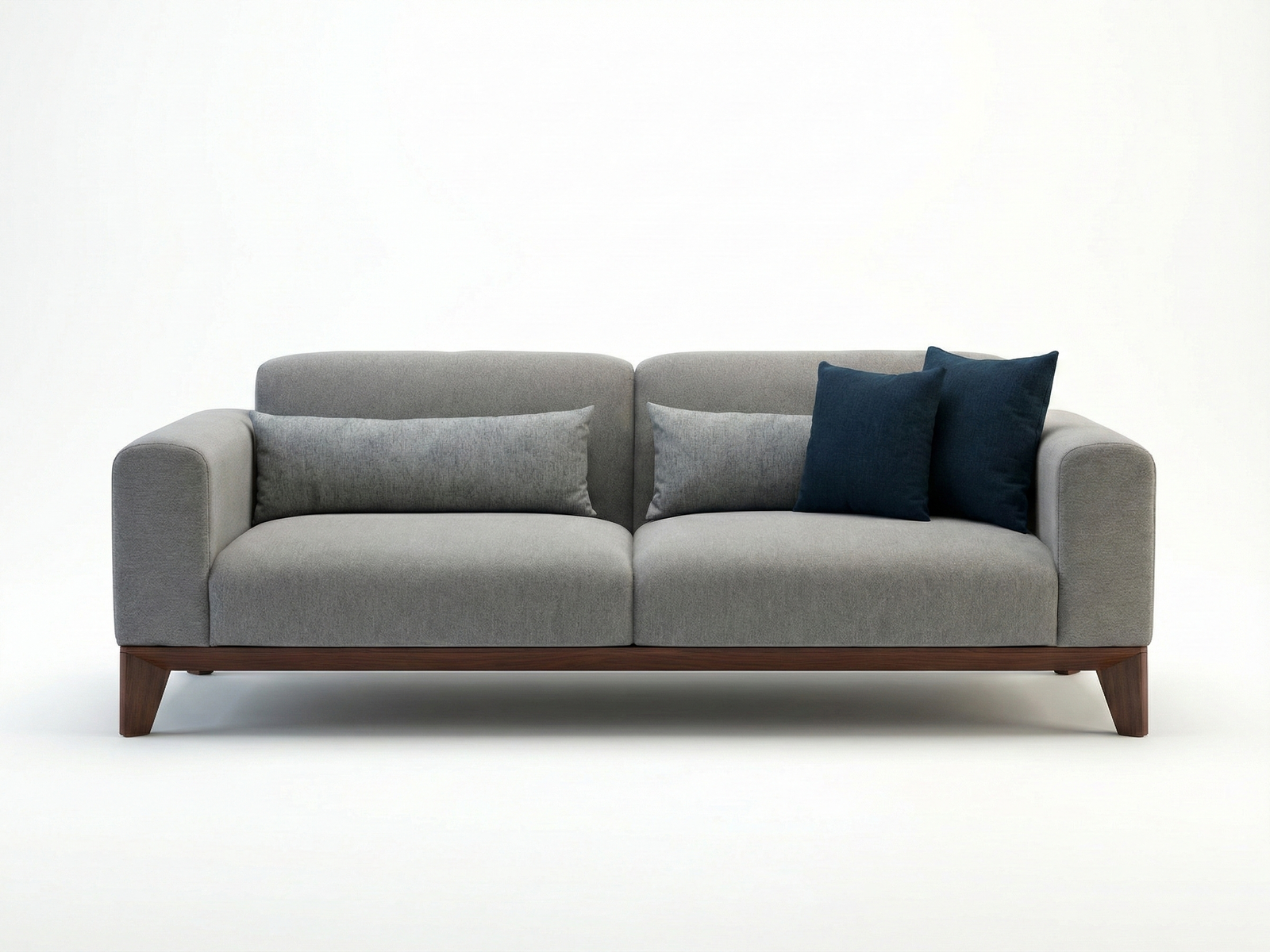 Front view of a modern Starling 3-seater sofa in grey fabric with a continuous Mahogany wood base, tapered legs, and navy blue accent pillows on a white background